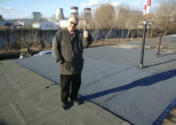 Заказчик в куртке показывает большой палец на готовой кровле, зимой, на фоне ТЭЦ